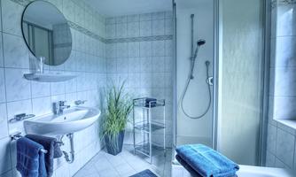 A modern bathroom with elegant tiles and a shower. On the shelf, there are towels and a plant adds freshness to the space.