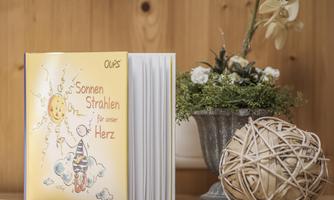A colorful book titled "Sunbeams for Our Heart" is on a table. Next to it is a decorative flower pot and a creative vine made of natural materials.