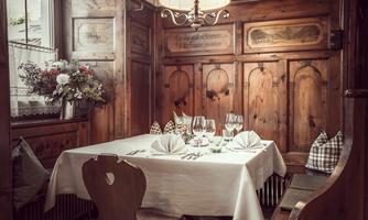 A rustic dining room with wood paneling and a beautifully set table. An elegant chandelier provides warm light and an inviting atmosphere.