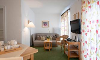 A bright living room with a comfortable sofa and a small table. Large windows with colorful curtains provide plenty of daylight.