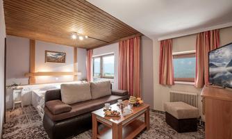A cozy hotel room with a double bed and a seating area. Large windows offer a beautiful view of the countryside.