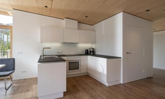 A modern, bright kitchen with white cabinets and a wooden floor. The equipment includes a stove, a refrigerator, and a coffee maker.