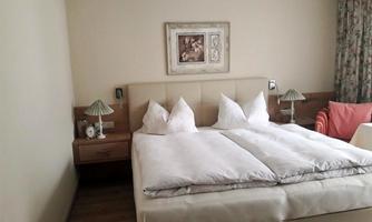 A cozy bedroom with a double bed and two nightstands. The room is bright and friendly with curtains and an armchair.