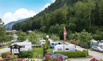 A campsite amidst green trees and mountains. Various RVs and tents are scattered across the grounds.