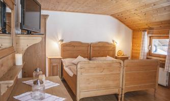 A cozy bedroom with wooden ceilings and two beds. There is a television and a pleasant, warm atmosphere.