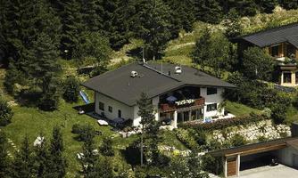 A modern house in a wooded environment. The garden is well-maintained and there is a terrace with flowers.