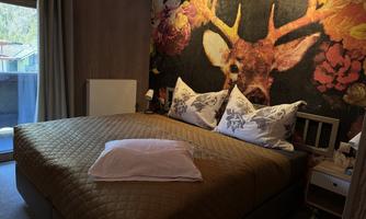 A cozy bedroom with a large bed and a beautiful wall design of a deer. The room has large windows and a friendly atmosphere.