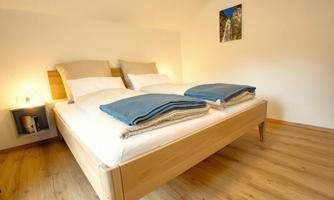 A modern bedroom with a large double bed and wooden floor. The ceiling is bright and there is a nice wall decoration.
