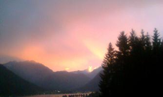 A picturesque landscape with mountains and a lake. The sky glows in soft pink and purple hues at sunset.