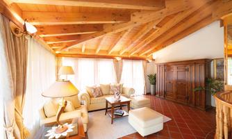 A bright living room with a wooden ceiling and large windows. It is cozily furnished with a sofa, a table, and a lamp.