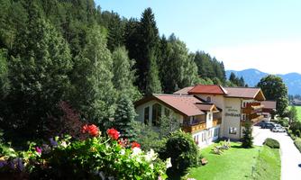 A picturesque landscape with a hotel and lush greenery. In the foreground, colorful flowers are blooming, and mountains can be seen in the background.