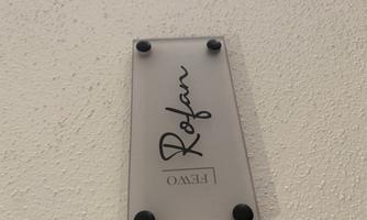 A decorative glass sign with the inscription "Rofan". It is attached to a white wall.