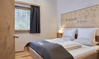 A cozy bedroom with a double bed and wood paneling. The window offers a view of nature, and the room is simply but stylishly furnished.