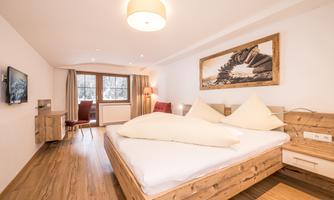 A cozy hotel room with a large bed and wooden furnishings. There is a window with a view and stylish lighting.