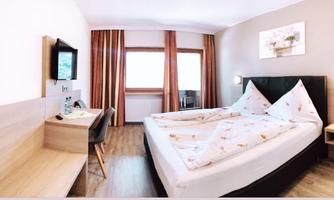 A modern hotel room with two beds and a desk. Large windows provide plenty of natural light.
