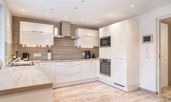 A modern kitchen with white cabinets and wood details. It is brightly lit and well organized.