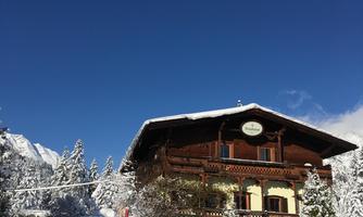 A charming chalet in the snow, surrounded by snow-covered trees. The sky is clear and blue.