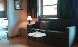 A comfortable living area with a sofa and a small coffee table. The windows let in plenty of daylight, and the atmosphere is inviting.