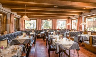 A cozy restaurant with a wooden ceiling and elegant tables. The windows offer a view of the outdoors and the atmosphere is inviting.
