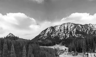 A picturesque mountain panorama with snow-covered peaks and wooded hills. The sky is covered with clouds.
