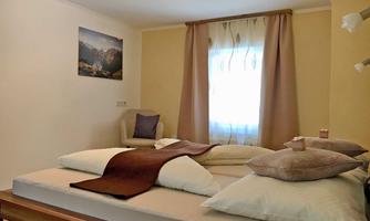 A cozy bedroom with two beds and beige walls. Curtains hang in front of a window, and a picture of a mountain landscape adorns the wall.