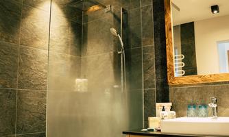 A modern bathroom with a glass shower and elegant stone wall. The wooden mirror and bright light sources give the space an inviting atmosphere.
