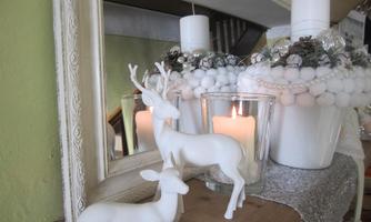 A decorative table with white animal figures and a candle. In the background, a mirror and a plant can be seen.