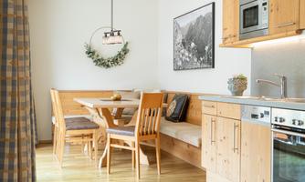 A cozy kitchen with wooden furniture and a dining table. A picture of a mountain landscape hangs on the wall.