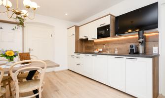 A modern kitchen with white cabinets and wooden details. The space is bright and inviting with a dining table and chairs.