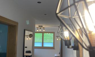 A modern hallway with stylish light sources and a large mirror. In the background, furniture and a window that lets in daylight are visible.