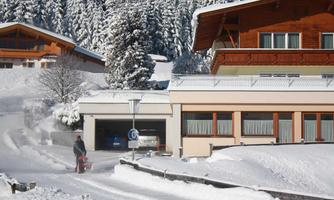 A snowy landscape with a house in the background. A man is clearing the snow with a snow plow.