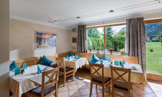 A cozy restaurant with bright wooden furniture and decorative tablecloths. Large windows offer a view of the green landscape.