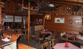 A cozy restaurant with wooden decor and traditional furniture. The tables are covered with checked tablecloths and there is ambient lighting.