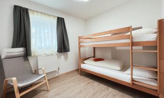 A simple room with a bunk bed and a comfortable chair. The window lets in plenty of daylight.