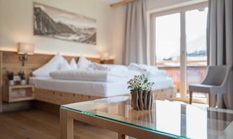 A cozy bedroom with a large bed and bright curtains. A table with a small plant arrangement stands in the foreground.