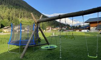 A beautiful playground with a trampoline and a swing. In the background, green meadows and mountains can be seen.