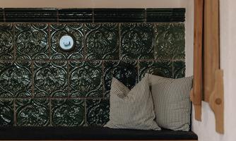 A cozy sitting area with a green tiled wall and two cushions. Wooden items are hanging on the wall for decoration.