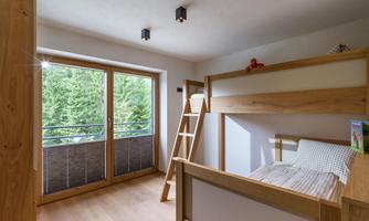 A modern children's room with a wooden loft bed and large windows. The room is bright and friendly, with a view of a green forest.