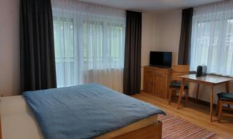 A cozy room with a large bed and a table.  
Large windows provide plenty of daylight.