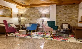 A cozy seating area with stylish armchairs in various colors. The room is decorated with a floral rug and standing lamps.