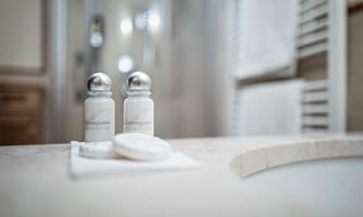 Two bottles of care products are on a small napkin in a bathroom. In the background, towels and a shower can be seen.