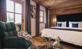A stylish room with a large bed and a cozy armchair. Large windows allow plenty of daylight to come in, creating an inviting atmosphere.