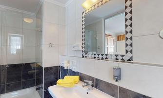 A modern bathroom with a glass shower cubicle and a sink. The mirror has a stylish frame, and yellow towels are ready.