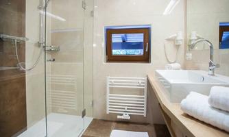 A modern bathroom with a glass shower and a double sink. Bright tiles and a large window create a friendly atmosphere.