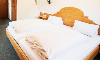 A cozy bedroom with a large wooden bed and fresh white bedding. The walls are clear and bright, which creates an inviting impression.
