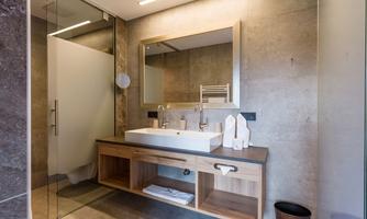 A modern bathroom with a wooden washbasin and a large mirror. The walls are made of smooth concrete, and the shower has an elegant glass partition.