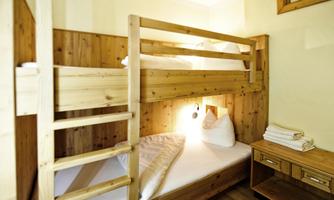 A cozy room with a wooden bunk bed and a single bed. There are soft pillows and fresh towels on a table.