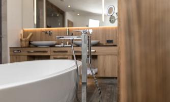A modern bathroom with a white bathtub and elegant wooden furniture. Soft lighting creates a calming atmosphere.