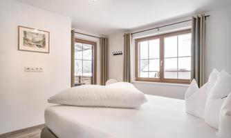 A cozy bedroom with a large bed and white pillows.  
Large windows provide plenty of daylight and a view outside.