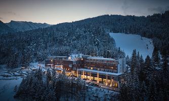 A modern hotel amidst a snowy landscape. Surrounded by trees and mountains, it exudes an inviting atmosphere.